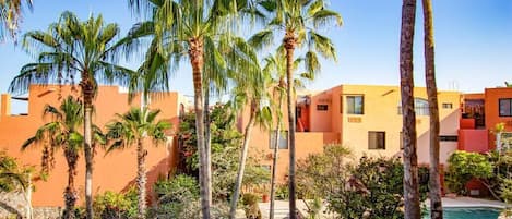 Un complexe hôtelier doté de palmiers, d’une piscine et de bâtiments modernes aux façades orange et beige.