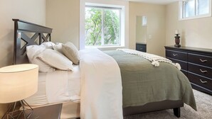 A bedroom with a bed, a nightstand, a lamp, a dresser, and a window with a view of trees.