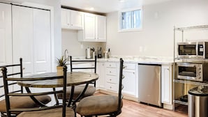 A compact kitchen with white cabinets, a dining table with chairs, a built-in oven, and a small window.