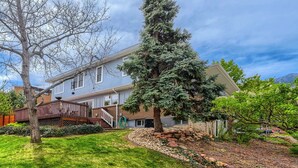 A two-story house with a stone foundation, a wooden deck, and a large evergreen tree.