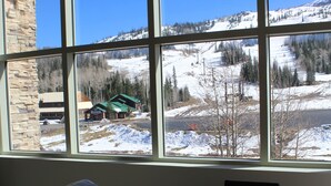 A room with a large window offering a view of a snowy landscape and a building across the street.