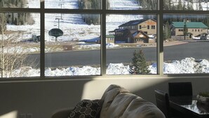 A room with a large window overlooking a snowy mountain landscape, a couch, and a dining table.
