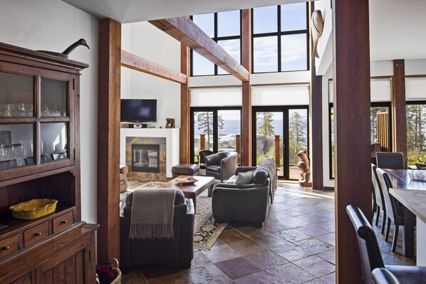A spacious living area with a fireplace, comfortable seating, and large windows offering a view of the ocean.