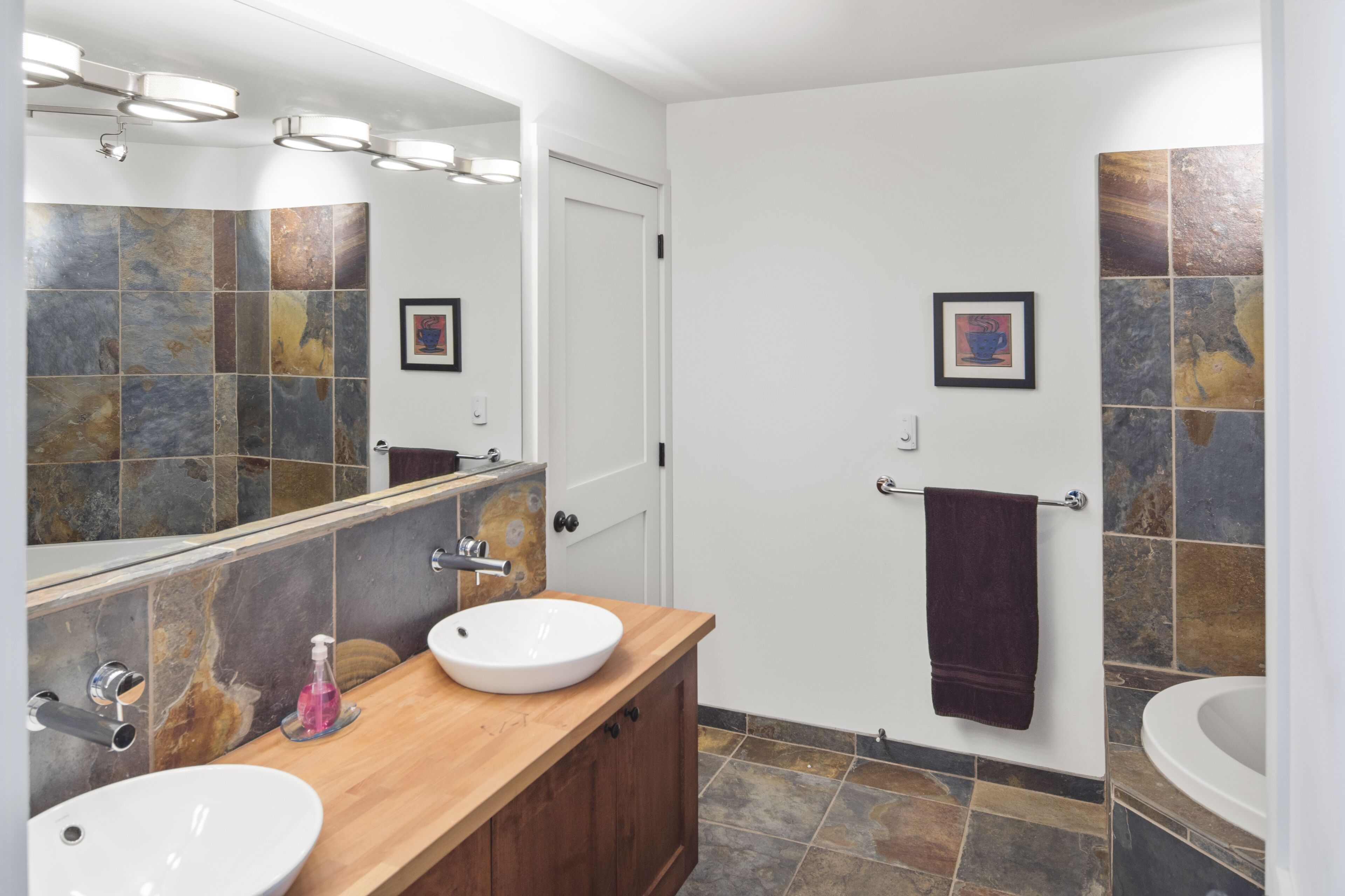 Casa de banho com duas pias, espelho e porta-toalhas.