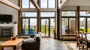 A spacious living room with a fireplace, a large window overlooking a deck, and a view of the ocean. - Ocean View Property - Black Rock Ridge (Ucluelet)