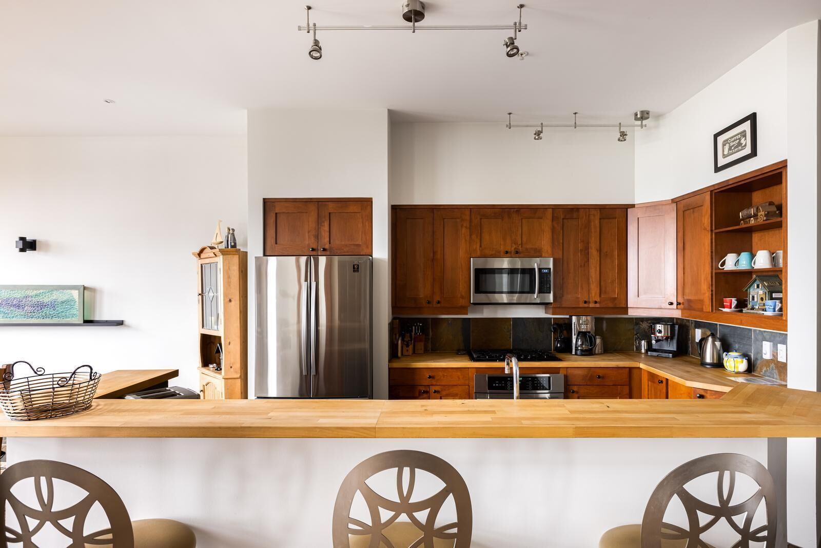 A modern kitchen with wooden cabinets, stainless steel appliances, and a wooden countertop.