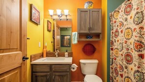 Een badkamer met een houten deur, een wastafel met spiegel, een toilet en een douchegordijn met bloemenmotief.