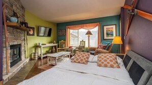 Een knus ingerichte kamer met een stenen openhaard, een bed met gestreepte kussens, een tafel met stoelen en een raam met gordijnen.