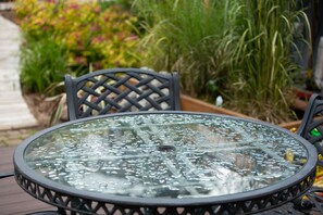 Une table ronde en verre, dotée d’un cadre en métal, entourée de chaises dont le dossier est orné d’un motif en croisillons.