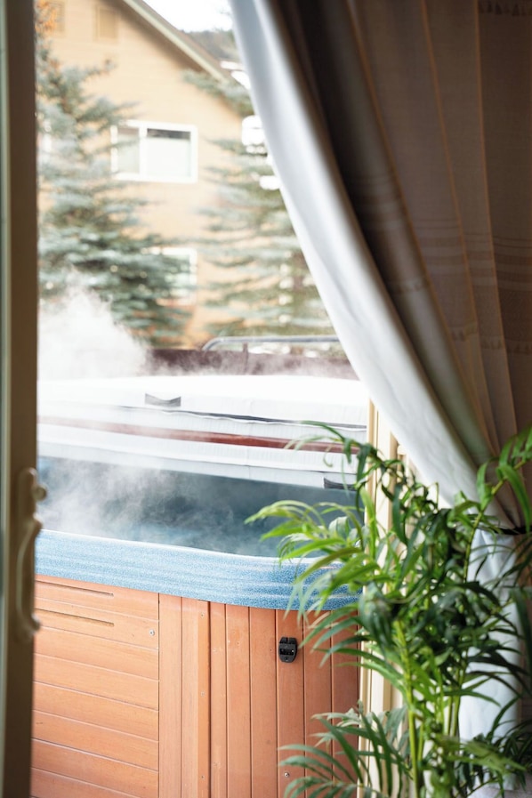 A hot tub with steam, a wooden deck, and a potted plant.