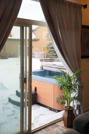 Habitación con puerta de vidrio corredera que da a un área exterior nevada, un jacuzzi de madera y una planta en maceta.
