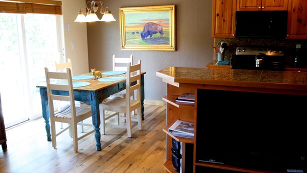 Un comedor con mesa y sillas de madera, un cuadro en la pared y una cocina con estufa y microondas.