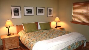 Una cama bien hecha con ropa de cama floral, dos mesitas de noche con lámparas y cuatro cuadros en la pared.