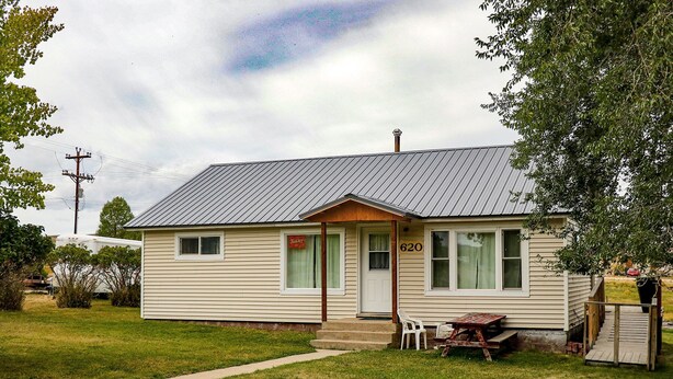 A single-story house with a number 620 on the front door, a small porch with a table and chairs, and a grassy yard. - All You Need Is Personal Items And Food. (Encampment)