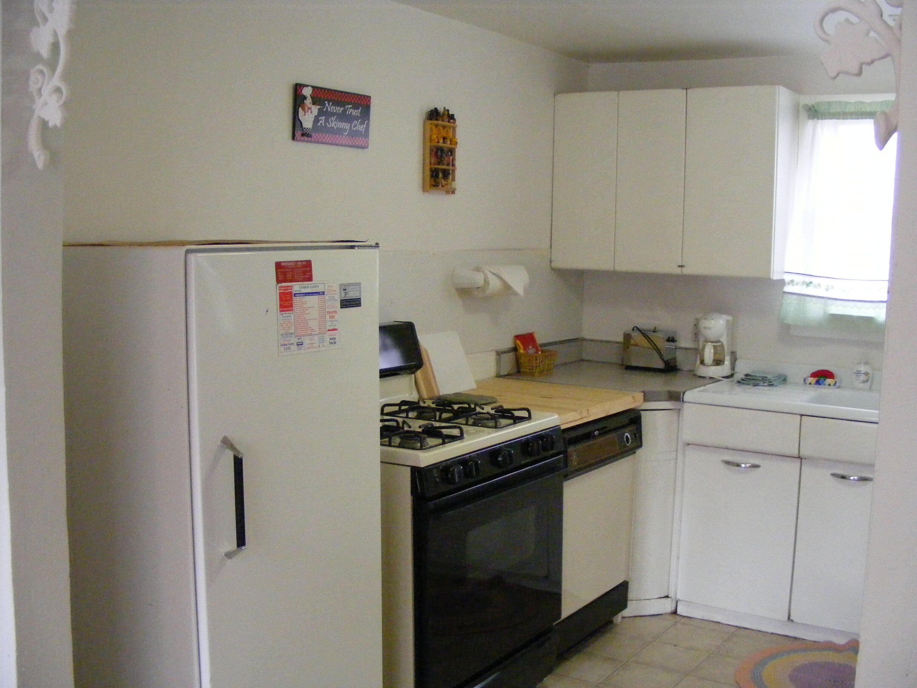 A compact kitchen with a refrigerator, stove, oven, and white cabinets.
