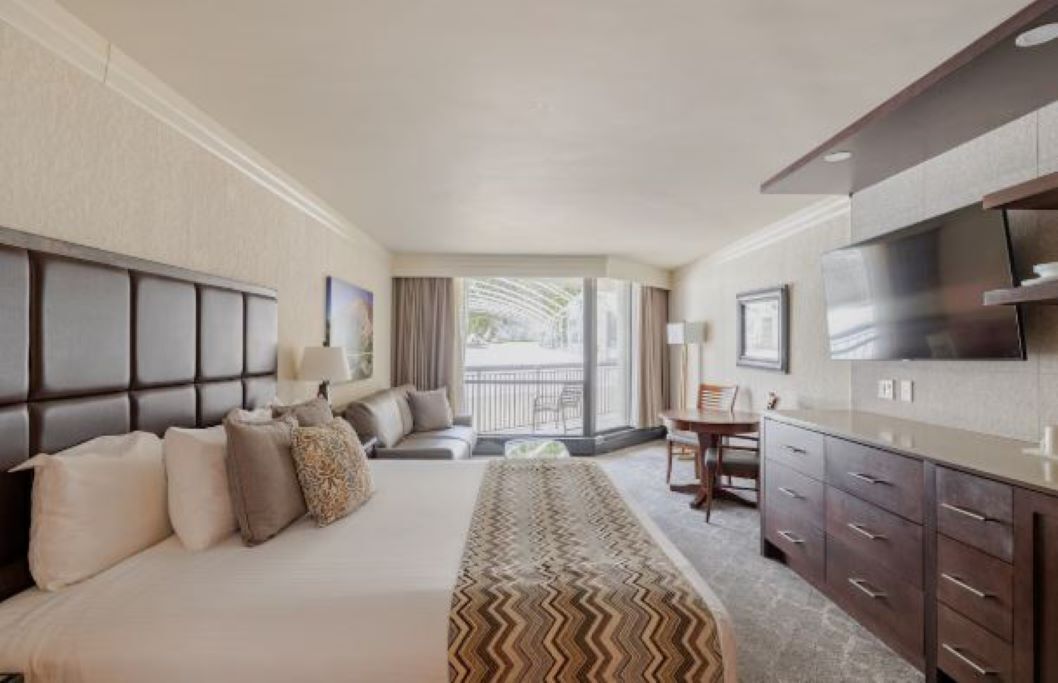A hotel room with a bed, a sofa, a dining table, and a TV.