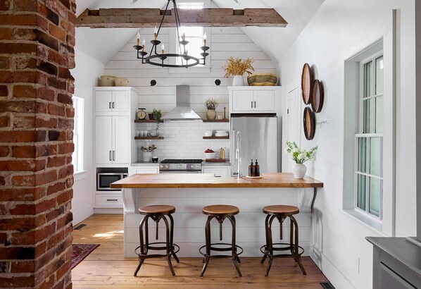 Una cocina con isla de madera, armarios blancos y pared de ladrillo.