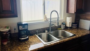 A kitchen with a double stainless steel sink, a coffee maker, and a window with a view of the outside. - Waterfront Luxury- 3 Plus Bedrooms (Clearlake Oaks)
