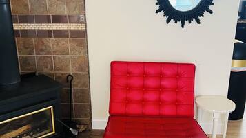 Una habitación con una butaca tapizada de rojo, una chimenea negra y un espejo redondo en la pared.