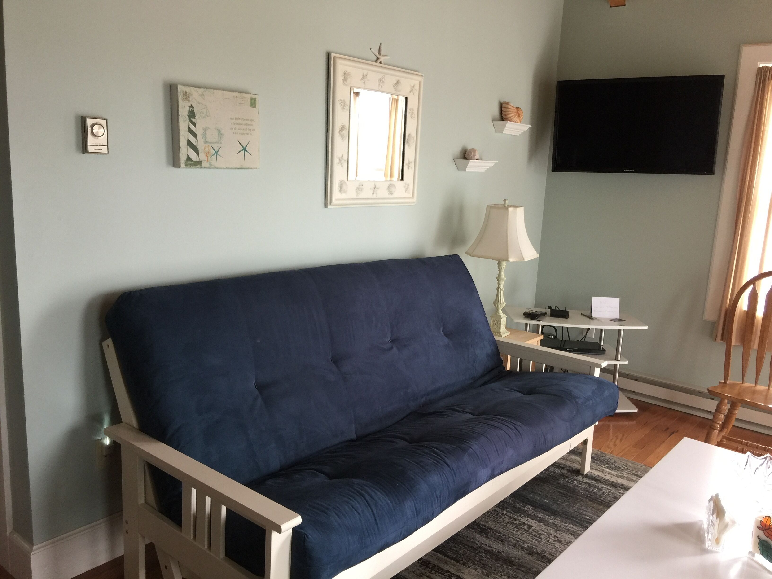Un salon avec un canapé bleu foncé, un téléviseur à écran plat fixé au mur, une petite table avec une lampe et un fauteuil.