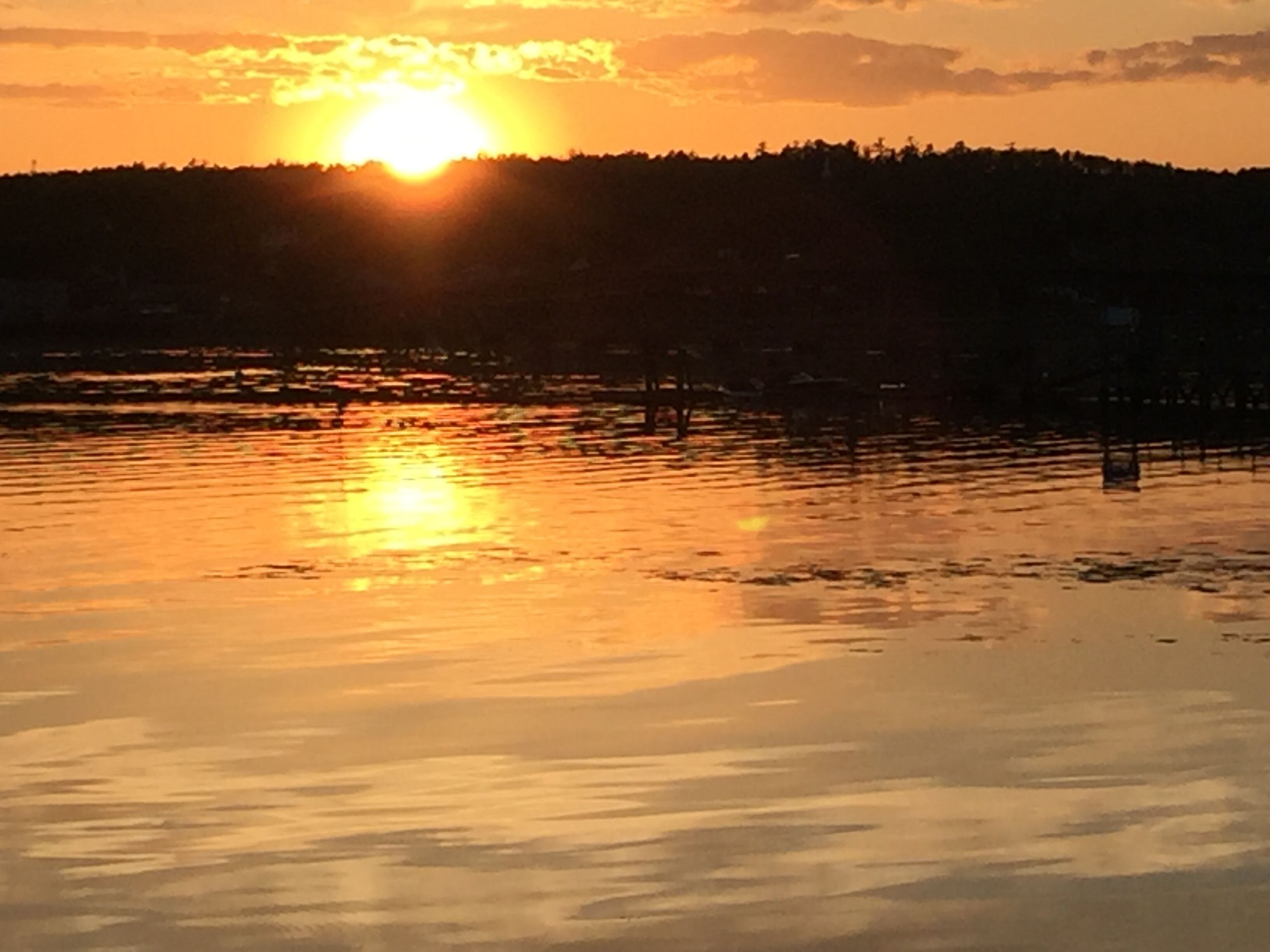A sunset over a calm body of water with a silhouette of a forested hill in the background.