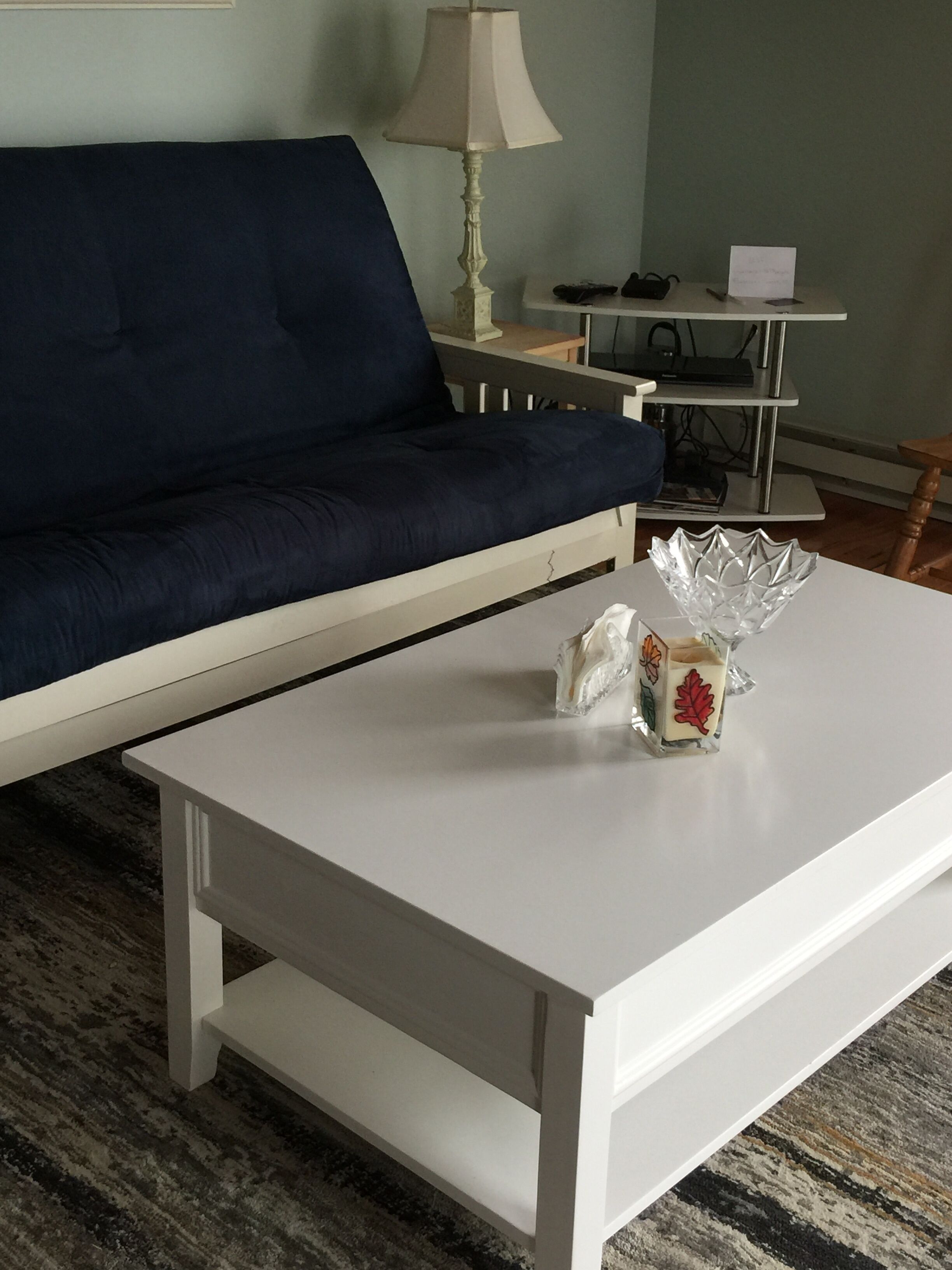 Une pièce avec un canapé bleu foncé, une table basse blanche surmontée d’un bol décoratif en verre, et une lampe sur une table d’appoint.