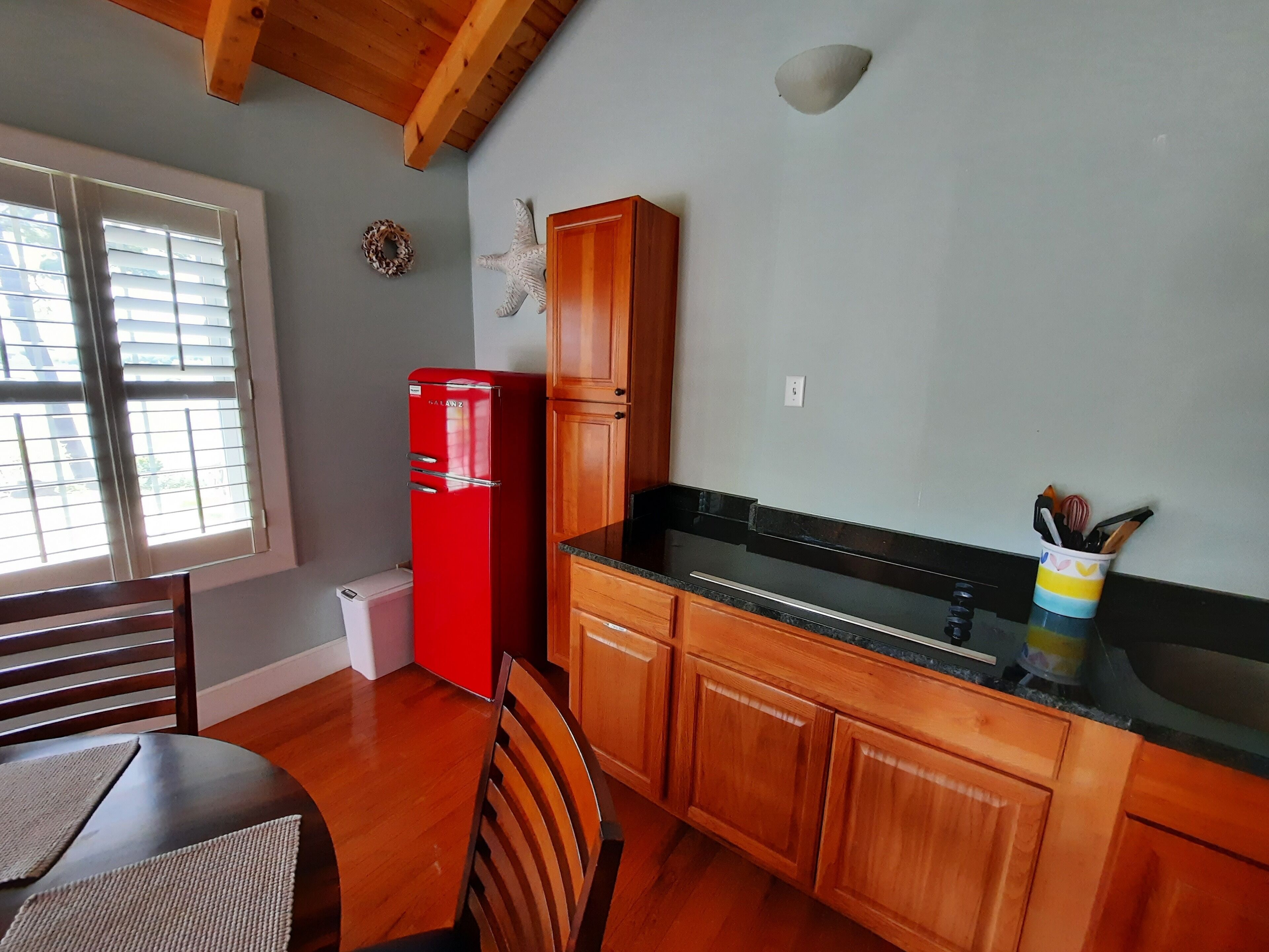 A compact kitchen with wooden cabinets, a red refrigerator, and a dining area with a table and chairs.