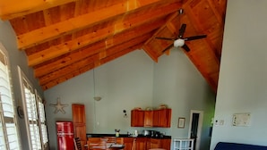 Een ruime loft met hoge plafonds, houten balken, een eethoek, keuken en een woonkamer met een blauwe bank en een witte salontafel.