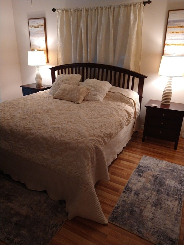 A neatly made bed with a wooden headboard, two bedside tables with lamps, and a window with curtains.
