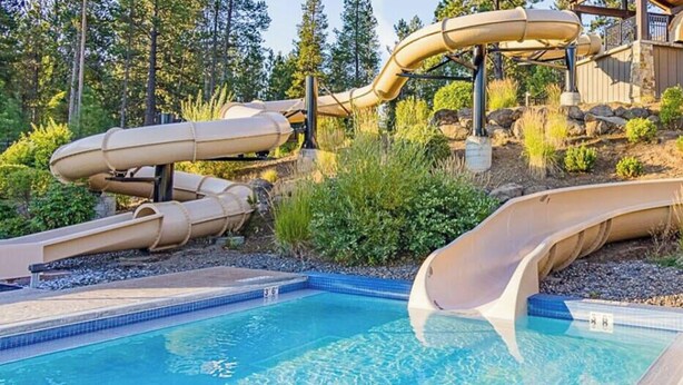A pool with multiple slides and a wooden deck. - Sunriver Gem - SHARC Pass |  Hot Tub |  Fireplace (Bend)