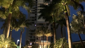 A nighttime view of a high-rise building with multiple balconies, surrounded by palm trees and illuminated by street lamps. - Direct Gulf Of America Views! (Marco Island)