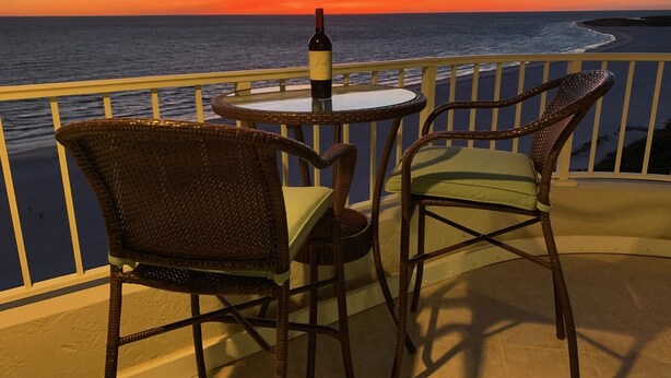 A balcony with wicker chairs and a table, overlooking a sunset over the ocean. - Direct Gulf Of America Views! (Marco Island)