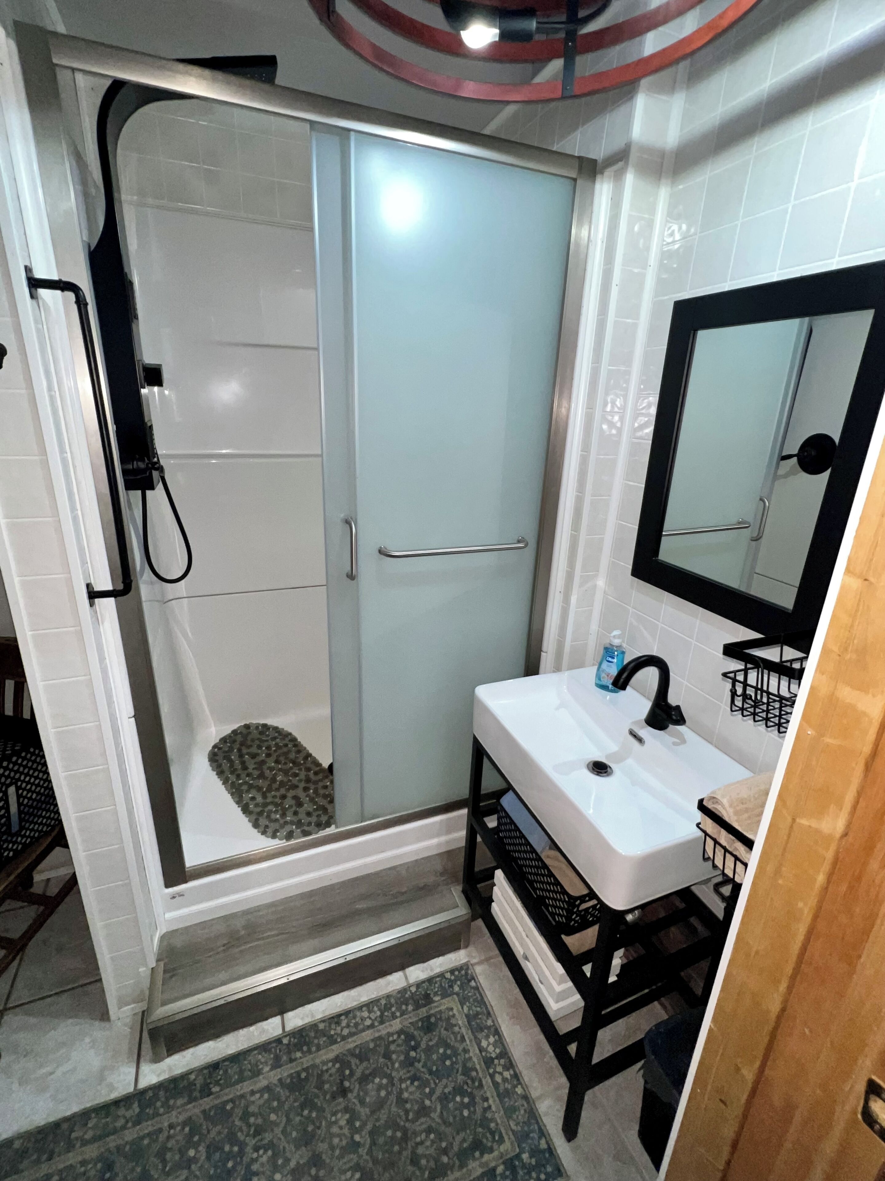 Une salle de bain avec une douche à parois de verre, un lavabo blanc avec un robinet noir et un miroir au-dessus du lavabo.