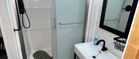 Une salle de bain avec une douche à parois de verre, un lavabo blanc avec un robinet noir et un miroir au-dessus du lavabo.