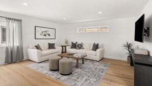 A modern living room with two sofas, a coffee table, and a TV mounted on the wall. - Ventura Beach House with Ocean View (Ventura)