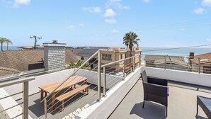 A rooftop terrace with a wooden table and chairs, overlooking a coastal area with buildings and a clear sky. - Ventura Beach House with Ocean View (Ventura)