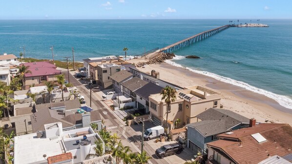 A coastal town with a pier extending into the sea, buildings along the beach, and a clear sky.