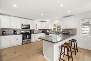 A modern kitchen with white cabinetry, a central island with stools, stainless steel appliances, and a window providing natural light.