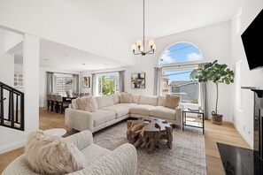 A spacious living room with a large sectional sofa, a coffee table, and a fireplace. There is a dining area with a table and chairs visible in the background.