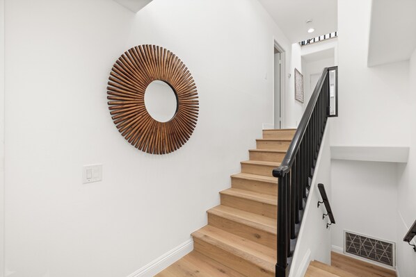 A staircase with wooden steps and a black railing, leading to a landing with a white wall and a circular wooden wall art piece.