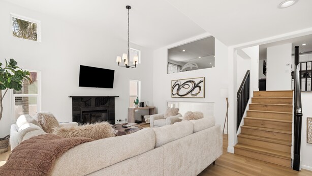 A modern living room with a large sectional sofa, a fireplace, a flat-screen TV, and a staircase leading to an upper level. - Ventura Beach House with Ocean View (Ventura)