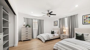 A bedroom with two beds, a dresser, a ceiling fan, and a window with curtains. - Ventura Beach House with Ocean View (Ventura)