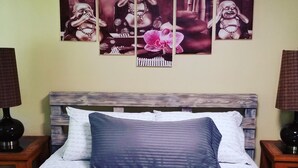 A bed with a blue pillow, a white towel, and a brown towel. There are two nightstands with lamps and a wall with four framed pictures. - Welcome to Sacred Pilgrimage Studio with Garden View. Pet-Friendly! (Victoria)