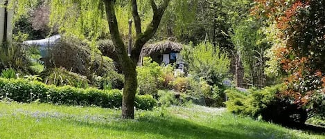 A lush garden with a tree, a thatched-roof structure, and various shrubs.