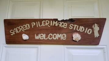 A wooden welcome sign with 'Sacred Pilgrimage Studio' text and two seashells.