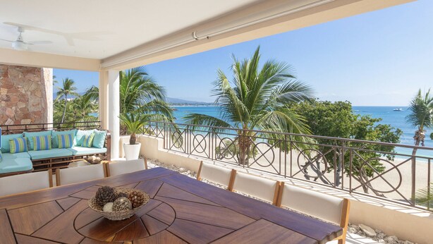 A wooden dining table with a decorative bowl, a light blue sofa with striped cushions, and a view of the ocean and palm trees. - Punta Mita Beachfront 5 star Luxury•Incredible VIEWS•PREMIER Membrsp. Golf Cart (Punta Mita)