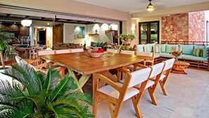 A spacious living area with a large wooden dining table surrounded by white chairs, a sofa with green cushions, and a stone wall. - Punta Mita Beachfront 5 star Luxury•Incredible VIEWS•PREMIER Membrsp. Golf Cart (Punta Mita)