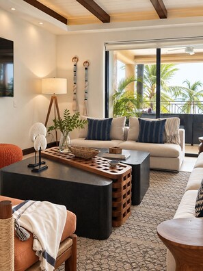 Ein modernes Wohnzimmer mit einer Couch, einem Couchtisch und Blick auf Palmen im Freien.