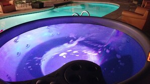A hot tub with a purple light, surrounded by outdoor furniture and a pool.