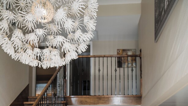 A spacious living room with a modern staircase, a large white sofa, and a unique chandelier.